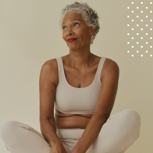 Woman in a beige tank top and white pants sitting on a beige background